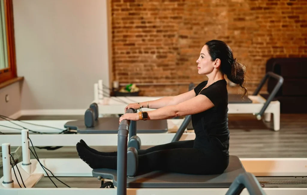 Woman practicing seated reformer stretch during a 30 minute Pilates workout for core and posture alignment