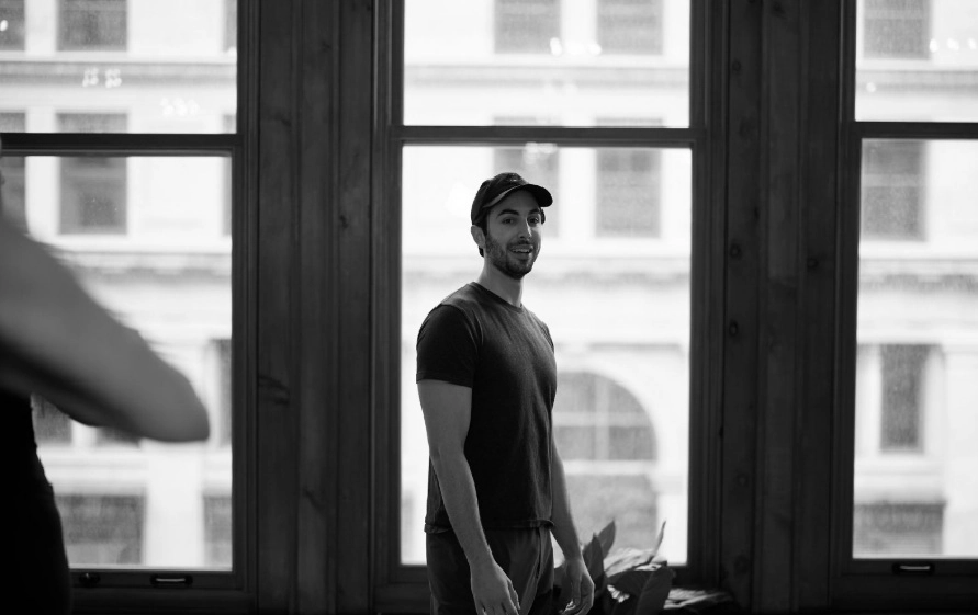 Smiling man in a t-shirt and baseball cap standing in a Pilates studio, looking happy and confident after a workout. Represents the positive experience of Pilates for men.