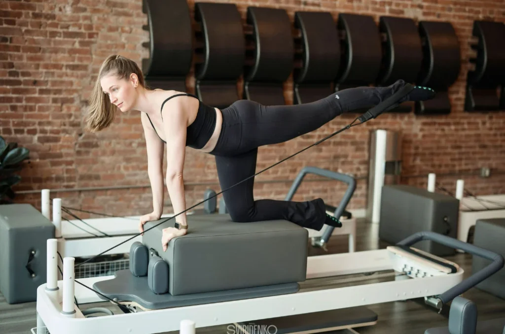 Female practitioner kneeling on a Pilates Box placed on a Reformer. Dynamic exercise on advanced Pilates Reformer equipment.