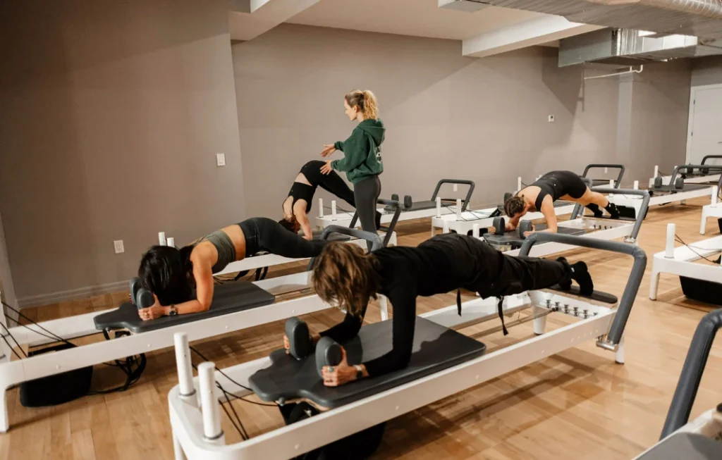Group reformer class with an instructor providing hands-on adjustments at a Pilates studio near me