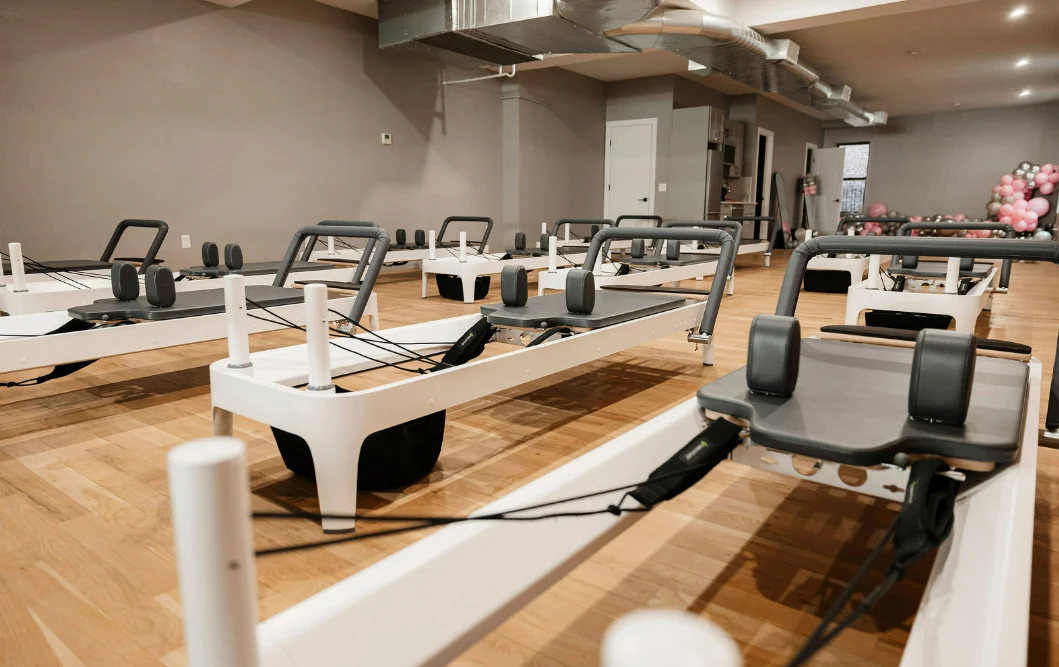 Row of professional white Pilates reformers in a spacious, sunlit studio