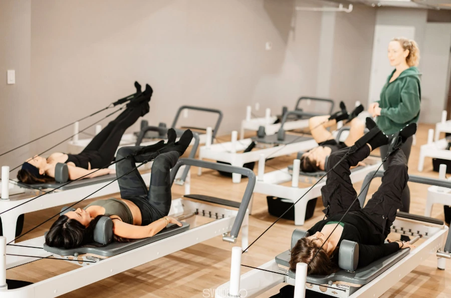 Clients performing a supine leg exercise using the straps on reformers during a class at BK Pilates