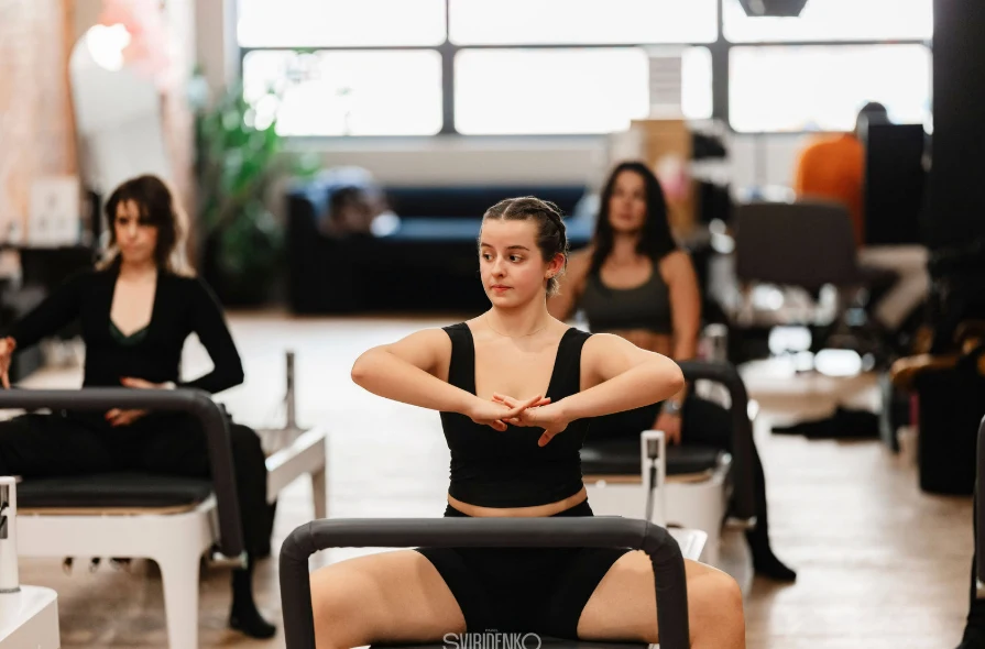 Young woman sitting on the reformer performing an arm and core strengthening exercise in a BK Pilates class