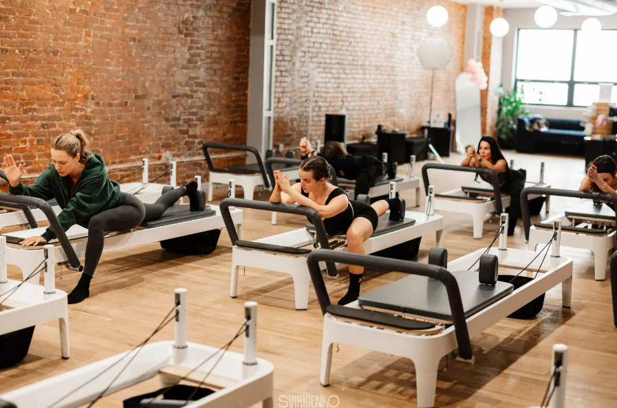 Group Pilates reformer class at BK Pilates Chelsea studio, featuring a stretching or squatting exercise