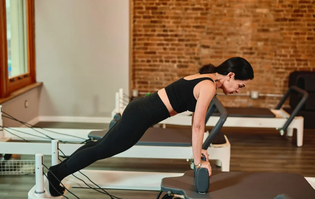 A woman in athletic wear performing a plank exercise on a Pilates reformer, demonstrating core strength during a personal training session.