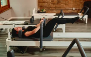 Side view of a woman performing a targeted abdominal workout on a professional Pilates reformer machine.