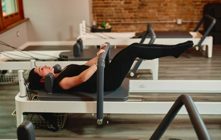 Side view of a woman performing a targeted abdominal workout on a professional Pilates reformer machine.