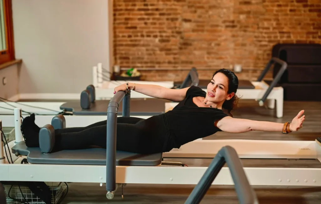A woman practicing a side-stretch exercise on a Pilates reformer at BK Pilates, focusing on core strength and flexibility