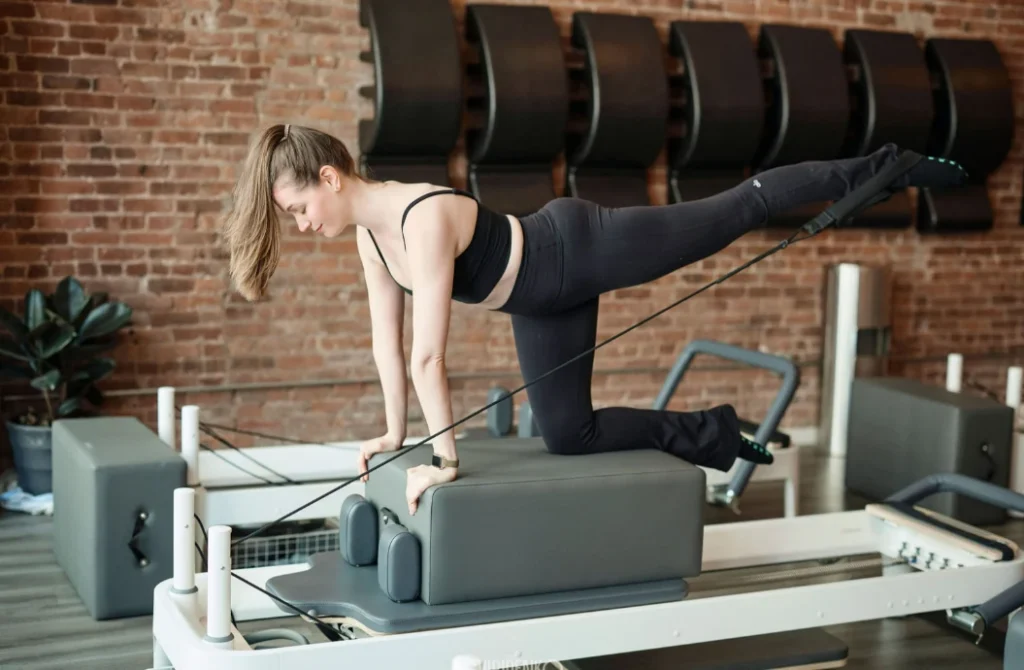 A woman performing a controlled leg extension on a Pilates reformer box at BK Pilates NoMad. She is focusing on core stability and joint alignment, which is essential for dancers and hypermobile bodies