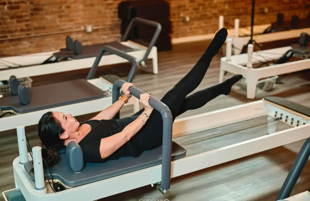 A woman engaging her core and lower body by pressing against the reformer bar. This image highlights the resistance-based training that causes post-workout muscle soreness in Pilates