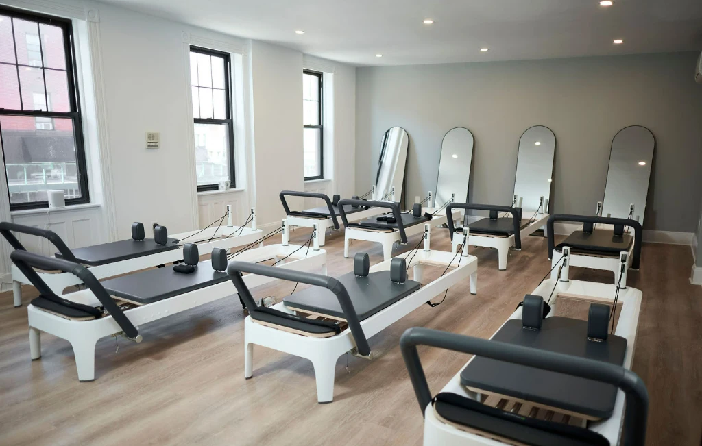 Bright and airy group Pilates class setting featuring multiple white Balanced Body reformers and arched mirrors in a modern NYC studio.