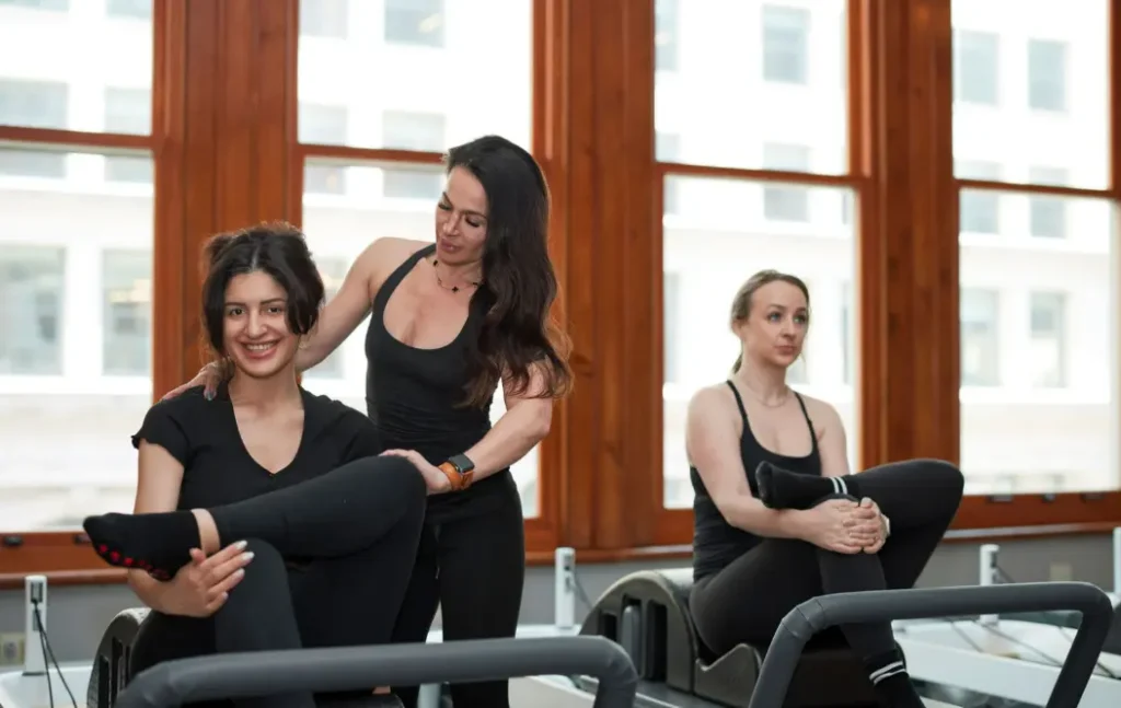 Close-up of a postpartum Pilates session where an instructor helps a client with alignment and core-focused movements on a reformer.