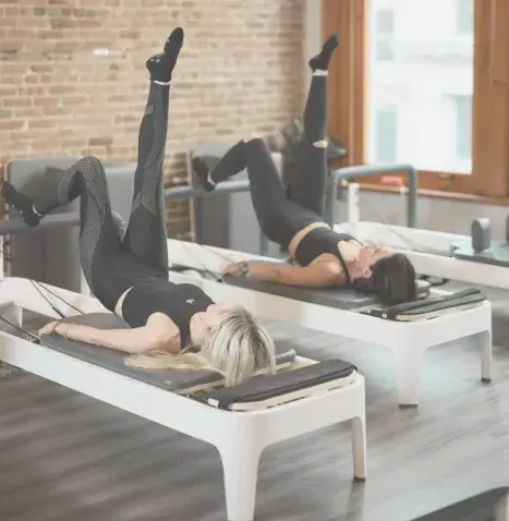 A dynamic duo Pilates class at BK Pilates studio, showing two women on reformers simultaneously performing a leg circle exercise, focused on glute and core strength