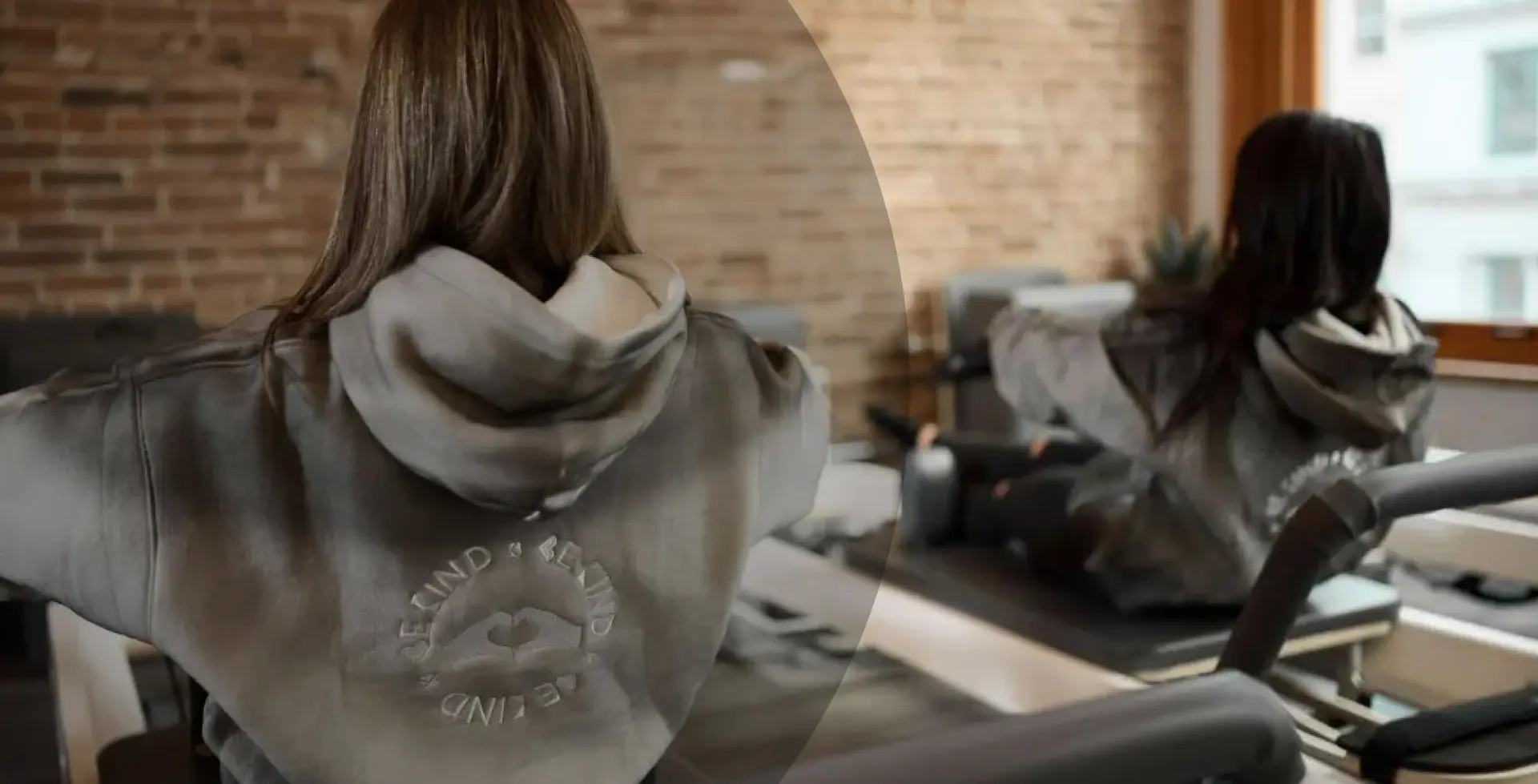 Pilates student wearing a "Be Kind" branded hoodie during a workout on a Reformer at BK Pilates Flatiron