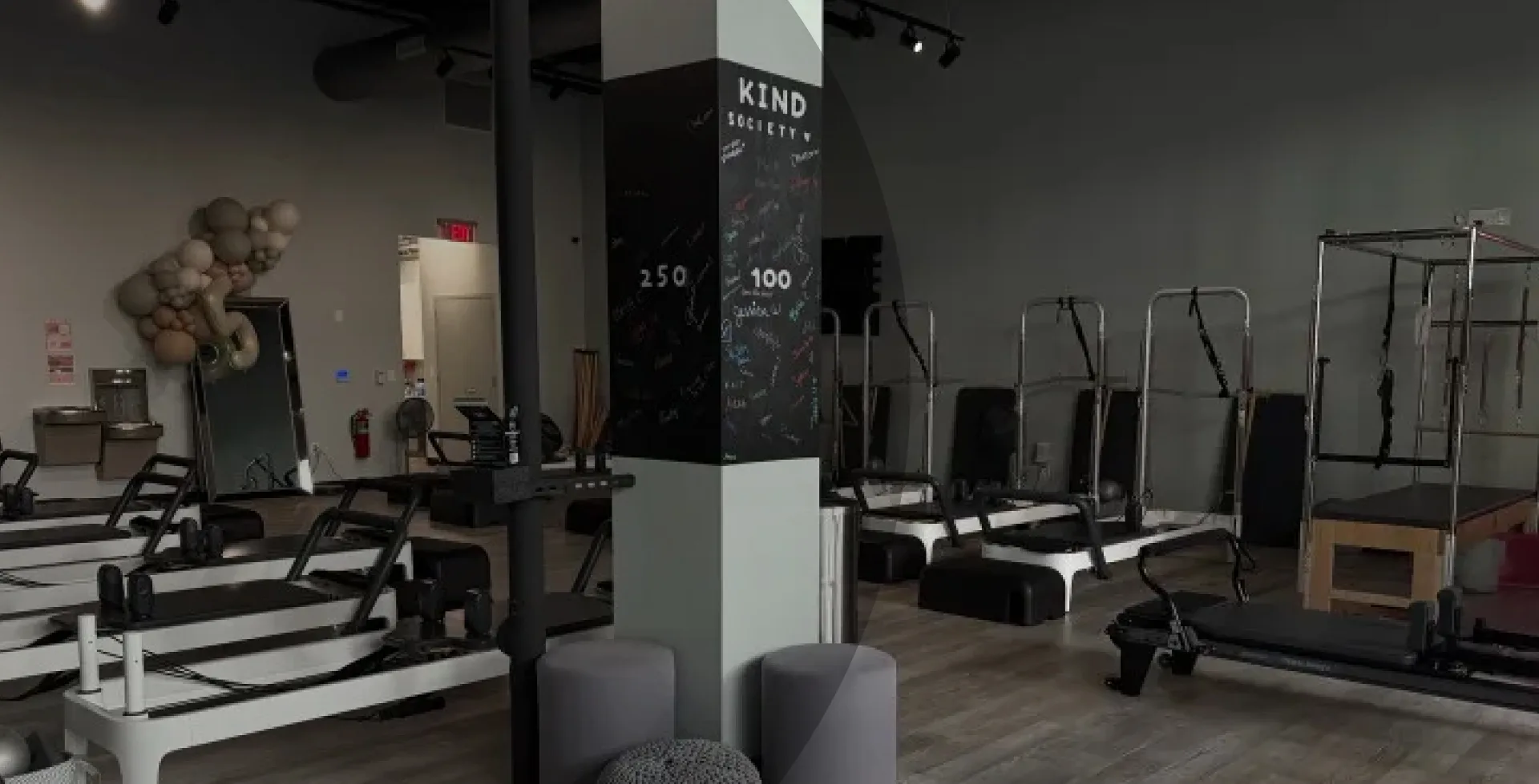 Modern Pilates studio at BK Pilates South End in Charlotte featuring rows of white reformers, sleek grey walls, a full-length mirror with a decorative balloon arch, and a prominent column wrapped