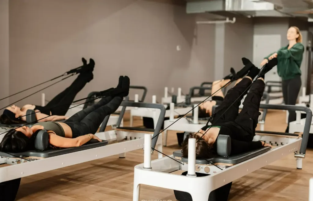 A group of women practicing core and leg styling exercises on beds during reformer pilates classes in NYC