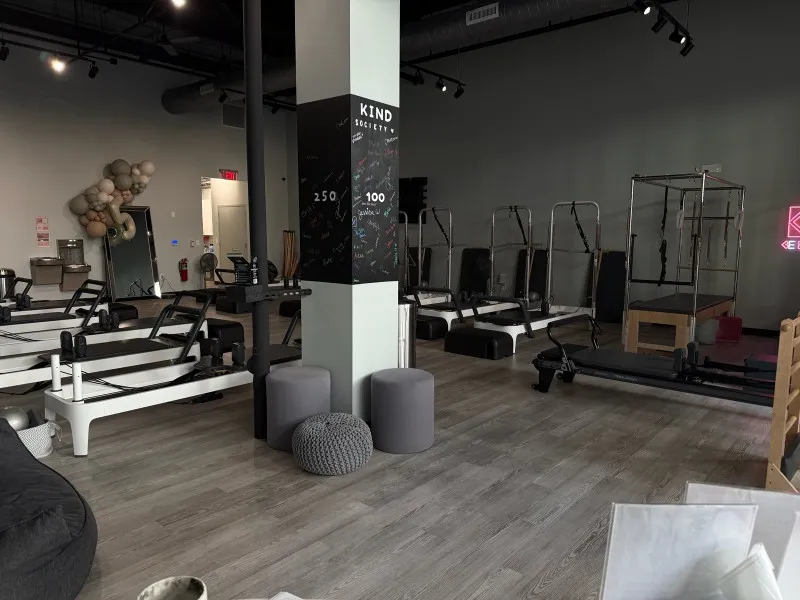 Inside look at BK Pilates studio in South Park showcasing a row of well-spaced reformer machines, a signature "Kind Society" chalk board pillar, and seating area