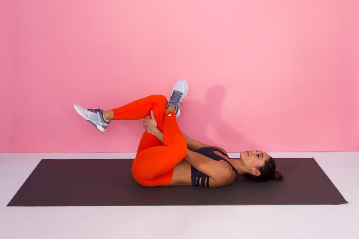 Woman doing a knee-to-chest stretch as part of an at-home stretching routine